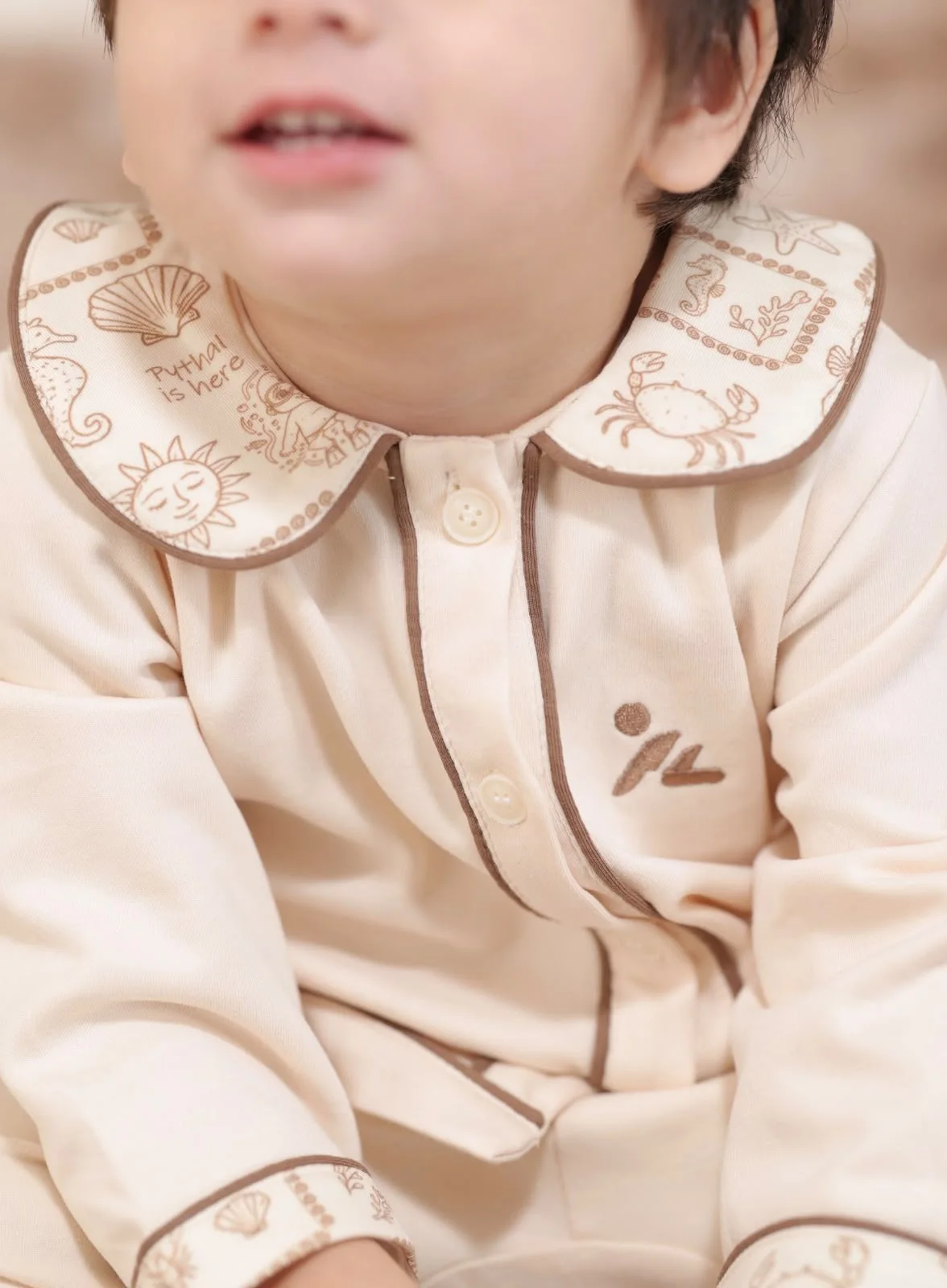 Close view of a child wearing a cream Pythal garment with illustrated collar details.