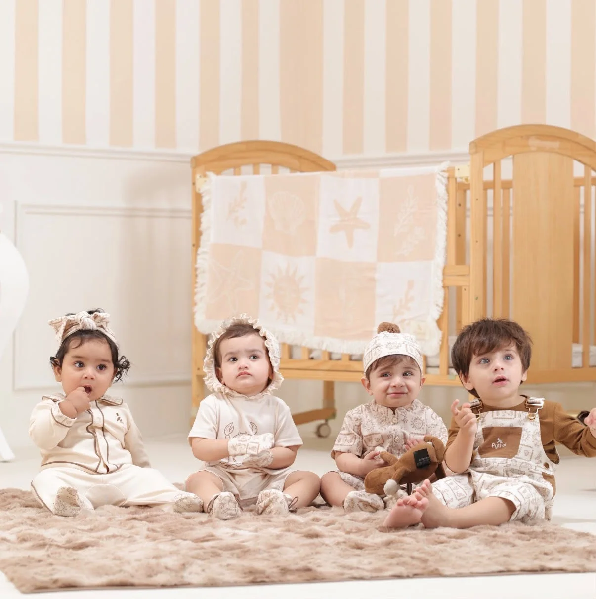 Four young children wearing neutral Pythal outfits seated together in a nursery.