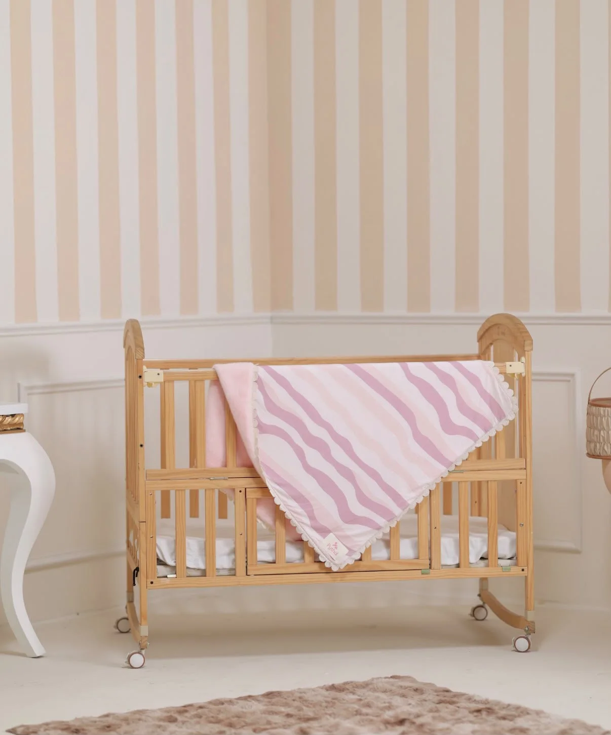 A Pythal pink striped blanket draped over a wooden nursery crib.