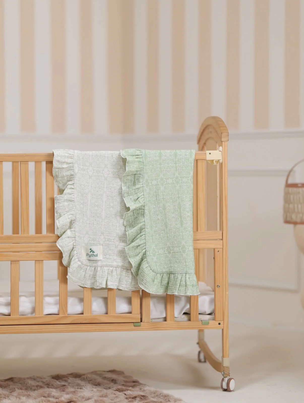 A Pythal sage and cream ruffled blanket draped over a wooden nursery crib.