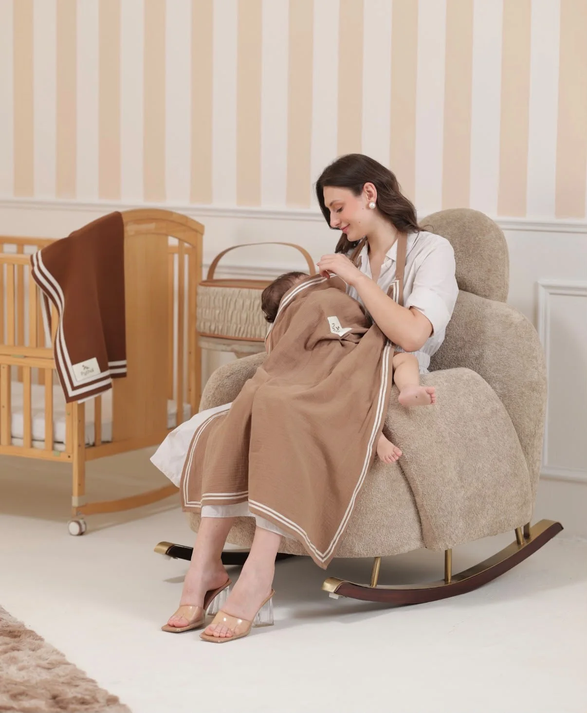 A mother holding her baby in a rocking chair with a Pythal blanket in a warm nursery.