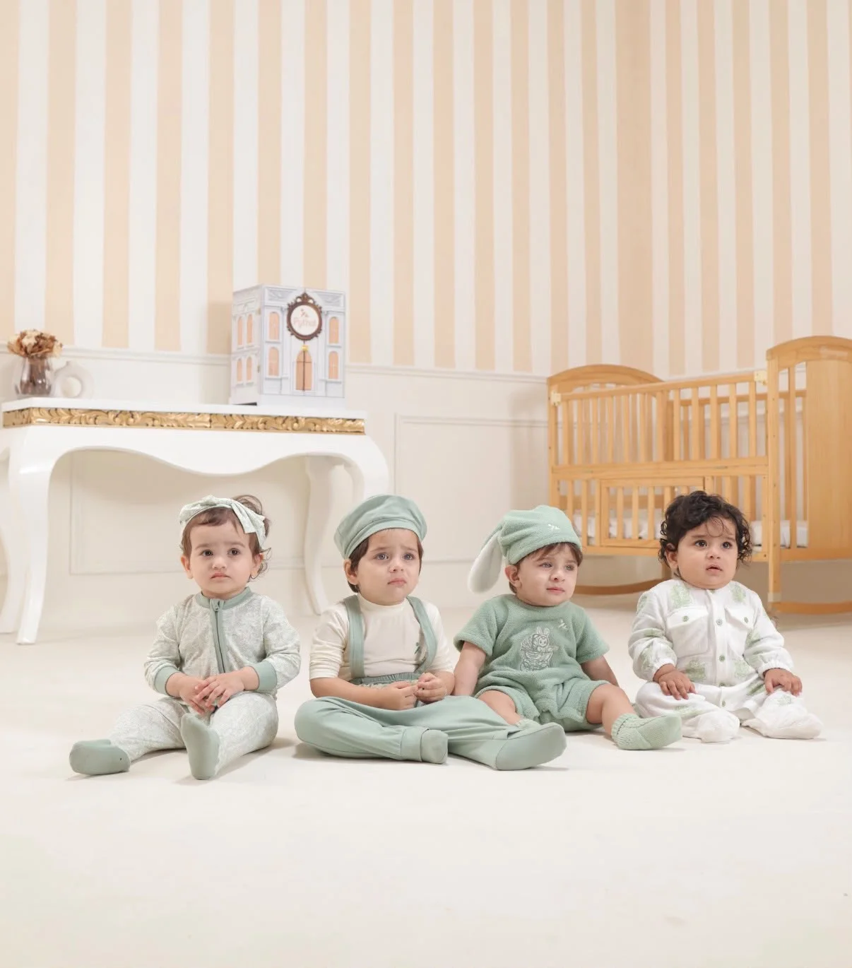 Four young children wearing soft sage Pythal clothing in a warm nursery.